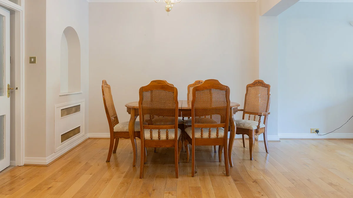 An outdated dining room interior before a professional makeover, showing a traditional dark wood dining set with cane-back chairs and bare white walls in a London property.