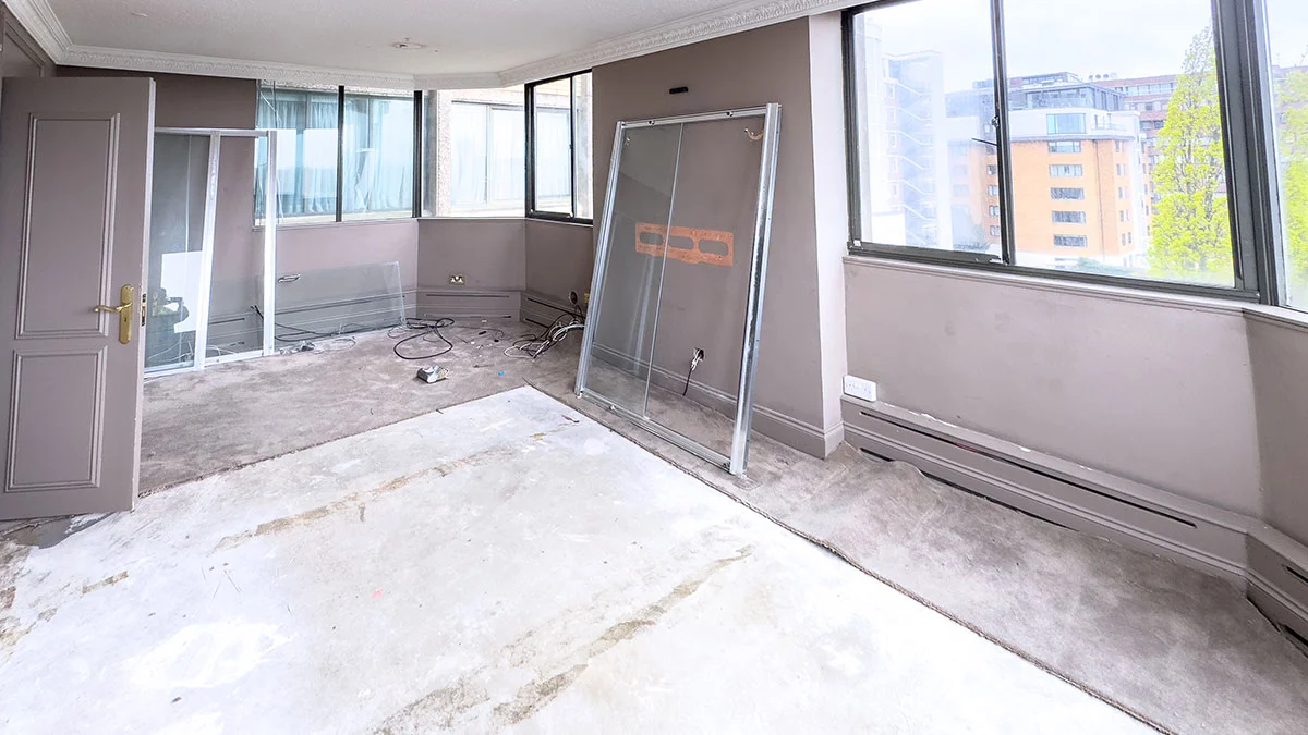 An empty apartment interior in St. John"s Wood during the renovation phase, showing stripped flooring, bare walls, and stored glass partitions before receiving professional interior styling.