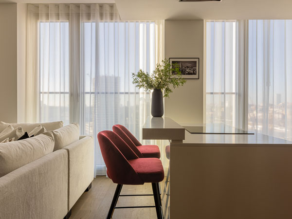 A bright modern space with soft sheer curtains, warm light, and a sleek seating area beside the kitchen counter