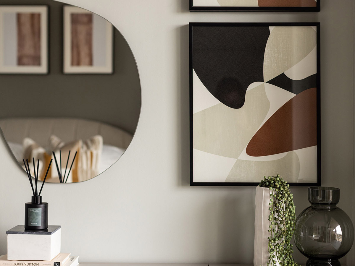 A chic arrangement of abstract art, a modern mirror, and decorative accents styled with thoughtfully curated show homes furniture