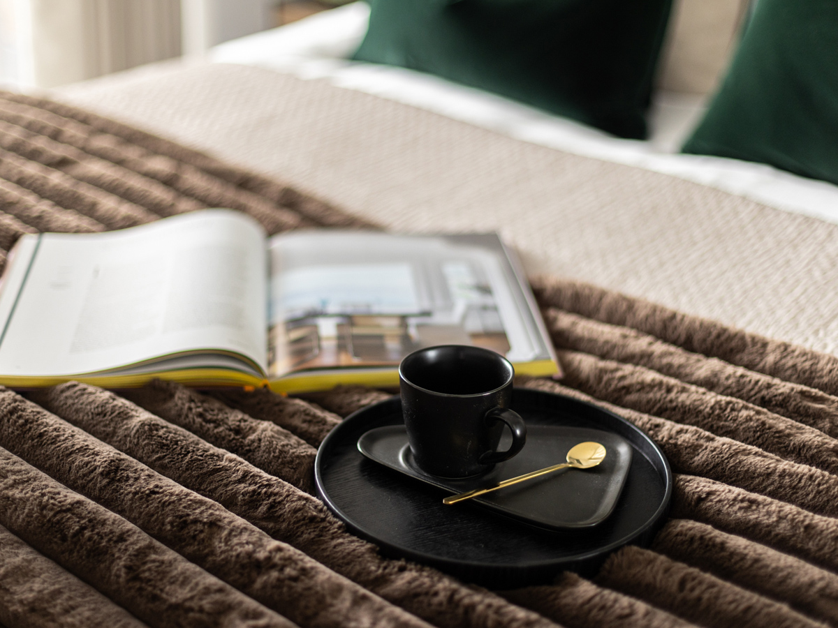 Cozy bedroom scene with an open book and a black coffee set on a textured blanket, showcasing the comfort and elegance of Instyle Direct bedroom furniture packages