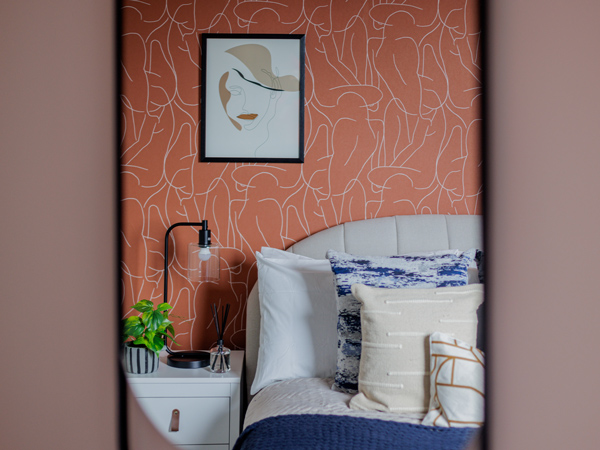 A modern bedroom featuring stylish Furniture Packages, including a cozy bed with layered pillows, a white bedside table, and contemporary wall art