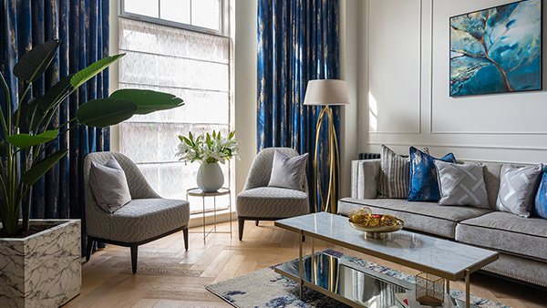 A bright, stylish living room with rich blue curtains and soft neutral seating, beautifully highlighting the impact of bespoke window dressing solutions
