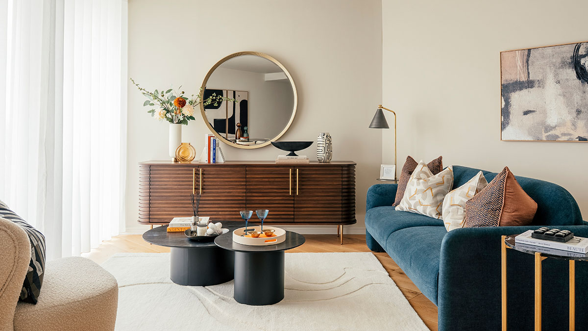 Modern living room with walnut sideboard, round mirror, teal velvet sofa, nesting coffee tables and neutral decor styling